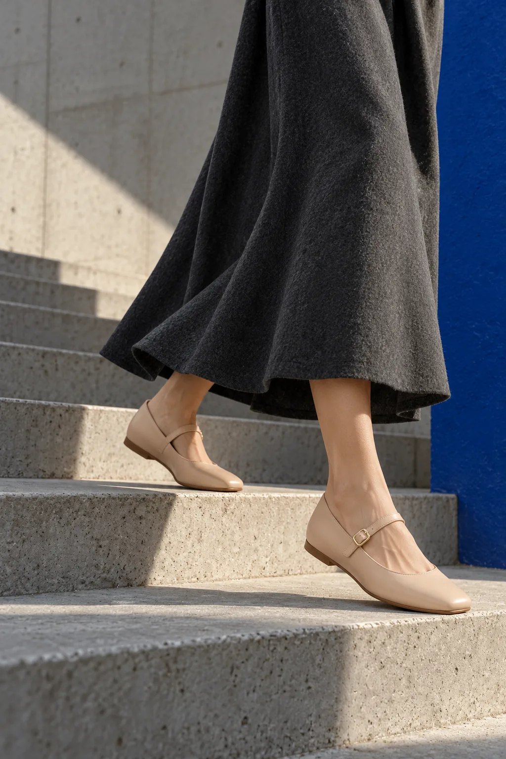 Nude leather Mary Jane flats on a concrete stair beside a cobalt wall